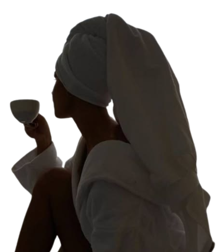 Femme en peignoir de 3/4 buvant un café et se détendant, serviette sur la tête.